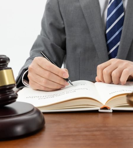 closeup-shot-person-writing-book-with-gavel-table-2-1-scaled.jpg